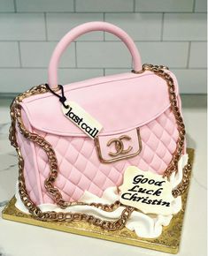 a cake shaped like a pink handbag with chains on it's sides and a name tag attached to the handle