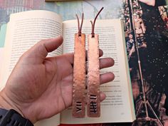 a person is holding two bookmarks in their left hand and an open book on the right