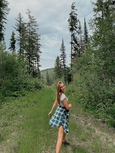 a woman in a plaid skirt is walking through the woods on a path with trees