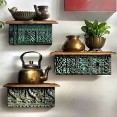 three metal teapots on wooden shelves next to a potted plant