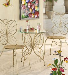 a glass table and two chairs in a room with flowers on the floor next to it