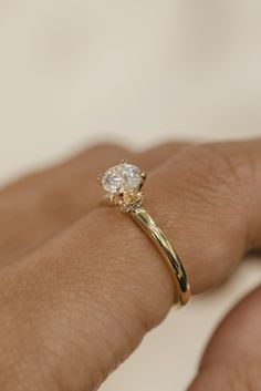 a woman's hand with a yellow gold ring on her left hand and a white diamond in the middle