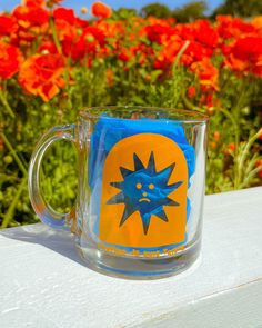 a glass coffee mug sitting on top of a white table next to red and orange flowers