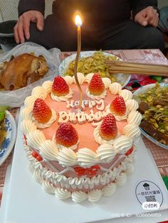 a birthday cake with strawberries on it and a lit candle in the shape of a heart