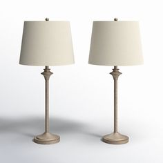 two lamps are sitting side by side on a white surface, one is turned off and the other has a beige shade