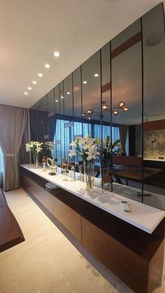 a long counter with vases and flowers on it in front of a large window