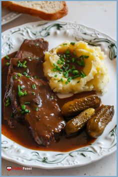 a white plate topped with meat and mashed potatoes covered in gravy next to bread