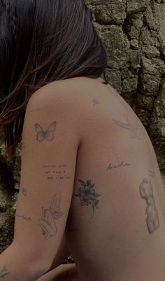 a woman with tattoos on her back sitting next to a stone wall and holding a cell phone