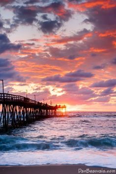 the sun is setting over the ocean with a pier in the foreground