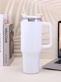 a laptop computer sitting on top of a desk next to a white cup and book