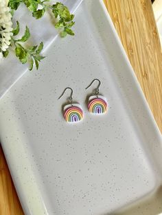 a pair of rainbow earrings sitting on top of a white tray next to some flowers