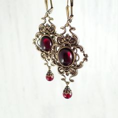 Romantic deep red Czech glass cabochons and Siam Red crystal beads paired with Victorian-style antiqued brass filigree. ------------------------------------------------------------------------------------------------------ Dimensions and details: - Cabochons measure 10x8mm - From the top of the ear wires to the bottom of the earrings, they measure approximately 2.4 inches (61 mm). - Settings and filigree are USA-made antiqued brass - Caps are USA-made antiqued brass-finished pewter - Cabochons a Red Vampire, Victorian Gothic Jewelry, Vampire Jewelry, Swarovski Crystal Beads, Accessories Diy Jewelry, Blood Red, Victorian Jewelry, Fantasy Jewelry, Gothic Jewelry