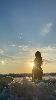 a woman standing in the ocean at sunset