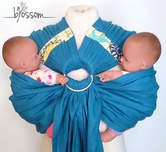 a baby wrapped in a blue wrap is held by an adult wearing a white shirt