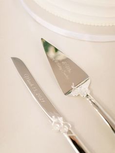 two silverware on a white table with a cake in the background and a wedding cake knife