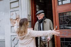 an older man and woman standing in front of a door with their hands out to each other