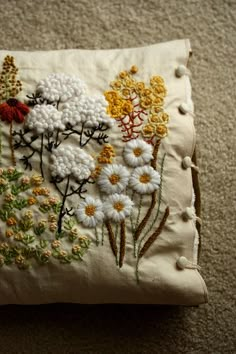 an embroidered pillow with flowers on it sitting on the floor in front of a carpet