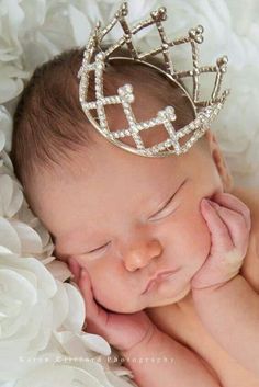 a baby wearing a tiara laying on top of white flowers