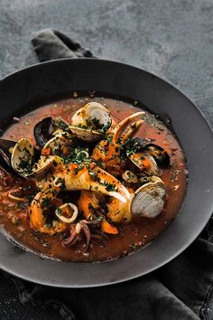 a bowl filled with seafood and clams on top of a black plate next to a napkin