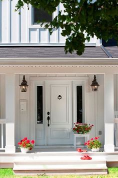 a white house with red flowers in the front and side window boxes on the porch