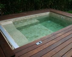 a wooden deck with an above ground swimming pool in the middle and green grass behind it