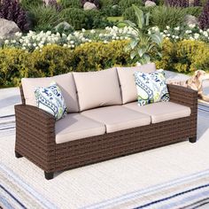 a couch sitting on top of a rug in front of a tree and bushes with blue and white pillows