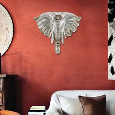 an elephant head mounted to the side of a red wall next to a white couch