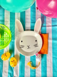 an easter bunny themed party with balloons, plates and rubber ducky toys on a blue and white striped tablecloth