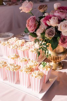 pink and white striped cupcakes are on a tray next to a gold vase with flowers