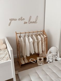 a baby's room with clothes hanging on the rail and a teddy bear next to it