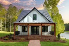 a white house with a porch and covered front porch next to a lake at sunset