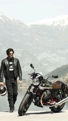 a man standing next to a motorcycle with mountains in the background