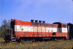 an old red and white train car sitting in the middle of a field with wildflowers