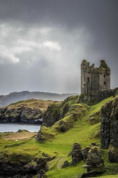 an old castle sitting on top of a lush green hill next to the ocean and mountains