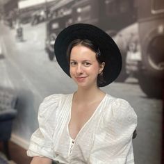 a woman wearing a black hat standing in front of a wall with cars on it