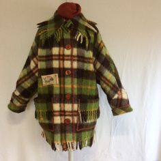 a green plaid coat with fringes on the shoulders and collar, hanging from a white wall