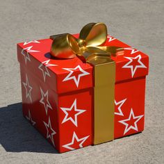 a red gift box with gold bow and star decorations on it sitting on the ground