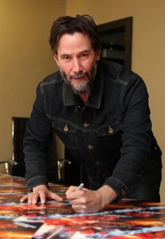 a man sitting at a table writing on a piece of paper with his hand in front of him