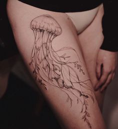 a woman's thigh with a tattoo of a jellyfish and leaves on it