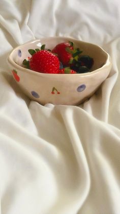 strawberries and blueberries in a bowl on a white bed sheet with polka dots