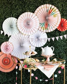 there are many paper umbrellas hanging on the wall behind a table with plates and cups