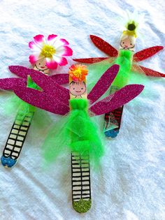 three colorful hair clips with tinkerbells and flowers on them sitting on a white sheet