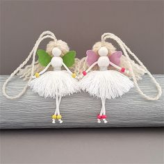 two small figurines are sitting on a piece of wood with white yarn and green leaves