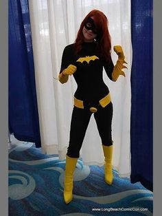 a woman dressed as batgirl standing in front of a window with blue drapes