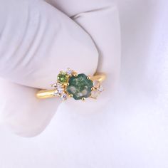 a close up of a person's hand wearing a ring with green and white stones