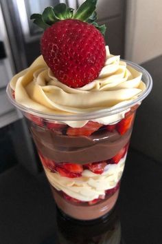 a chocolate trifle with strawberries and whipped cream in a plastic cup on a table