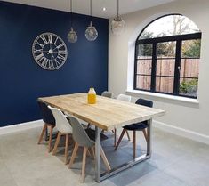 a dining room table with chairs and a clock mounted to the wall behind it in front of a window