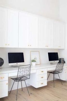 two computer monitors sitting on top of a desk next to each other in front of white cabinets