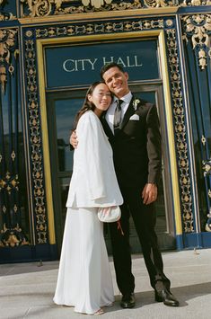 a man and woman standing in front of a city hall building with their arms around each other