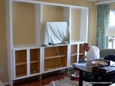 a man sitting in front of a tv on top of a wooden shelf next to a window